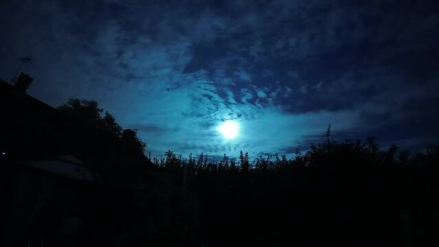 Timelapse footage of the full moon rising in blue dusk sky among the heavy clouds