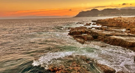 Deurstickers Ocean waves crashing against the rocky shoreline of Fish Hoek Beach in Cape Town, South Africa © Wirestock