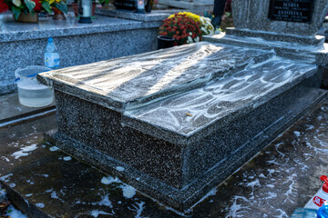Preparing a grave for All Saints' Day celebrated on November 1st, a woman cleans and washes a...