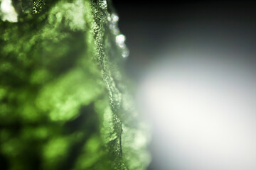 Tektite glass green texture. Moldavite gemstone close up. Lens flare. Light beam. Rough surface.