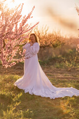 Woman blooming peach orchard. Against the backdrop of a picturesque peach orchard, a woman in a long white dress enjoys a peaceful walk in the park, surrounded by the beauty of nature.