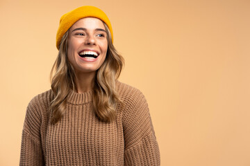 Attractive smiling woman wearing yellow hipster hat and stylish winter sweater isolated on beige background, copy space. Portrait of happy female tourist looking away. Inspiration, travel concept