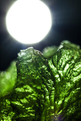 Tektite glass green texture. Moldavite gemstone close up. Lens flare. Light beam. Rough surface.