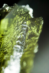 Tektite glass green texture. Moldavite gemstone close up. Lens flare. Light beam. Rough surface.