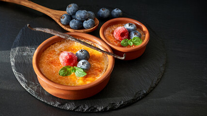 Creme brulee with raspberry, blueberry and mint leaves in terracota clay baking dishes on dark stone