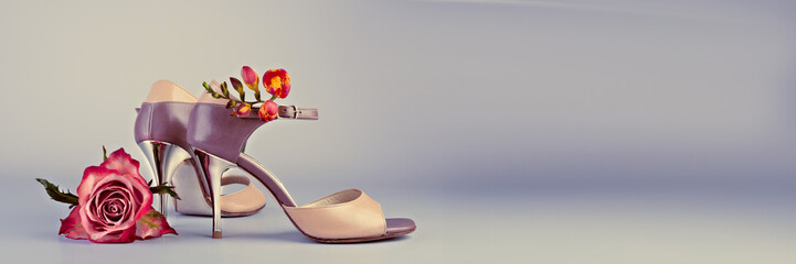 Stiletto tango shoes and flowers on grey background Panoramic banner image.