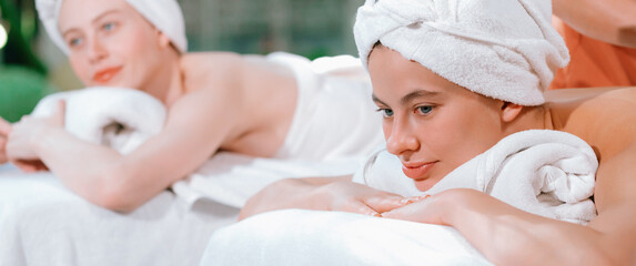 A portrait of a couple of a beautiful young caucasian woman with white towel rest on comfortable spa bed with relaxation while having body massage with professional masseur at spa salon.Tranquility. - obrazy, fototapety, plakaty