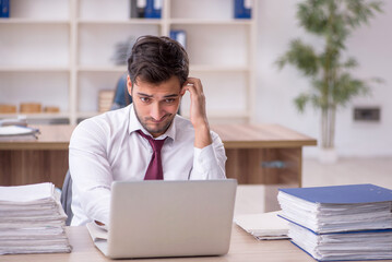 Naklejka premium Young male employee and too much work at workplace