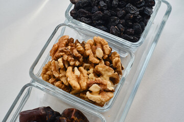 Raisins, nuts, dates in glass bowls on a white table. Concept of proper nutrition and sweets