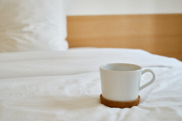 Fototapeta na wymiar White cup with coffee or tea on the bed. Cozy morning photo. The concept is cozy and warm. Place for text 