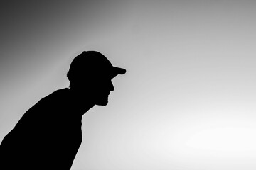 Grayscale low angle shot of a young male in a baseball cap silhouette looking into the distance