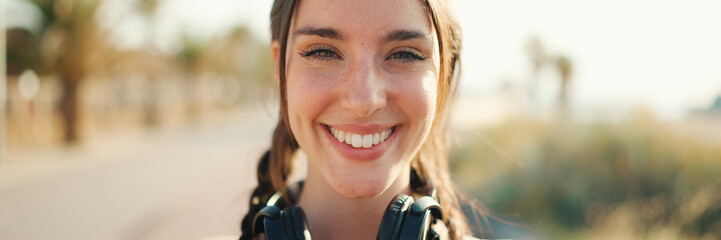 Cute young athletic woman with braided pigtail wearing beige sports top with headphones stands on...
