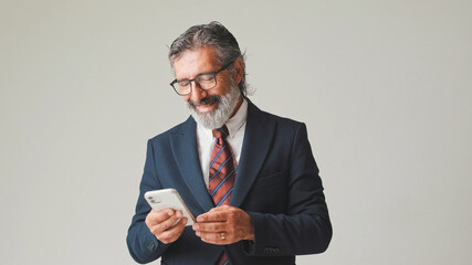 Businessman in glasses with gray hair, looking with smile at the screen of mobile phone, isolated...