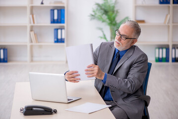 Old male employee sitting at workplace