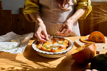 Autumn healthy eating. Woman preparing delicious seasonal tart with baked pumpkin, brie cheese and herbs.