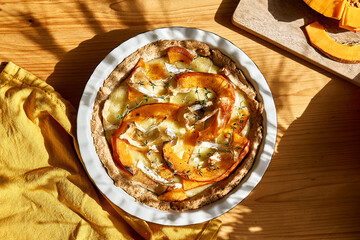 Autumn healthy eating. Delicious seasonal tart with baked pumpkin, brie cheese and herbs on wooden...