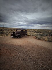 Obraz premium Vintage automobile parked along a scenic rural gravel road, with a backdrop of cloudy skies