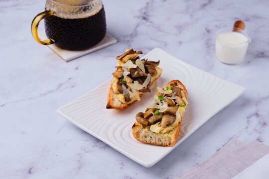 Sandwiches on a baguette with hummus, oyster mushrooms and parmesan cheese on a white ceramic plate on a marble background. Modern style in food photography, minimalism.