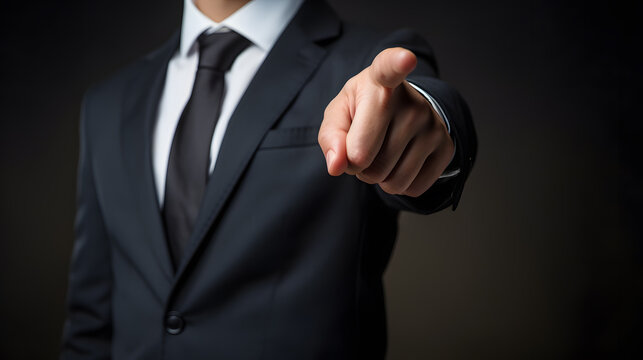 Businessman in a suit point finger at camera on black background
