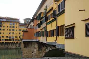 Fototapeta na wymiar Old Bridge over water in Florence, Italy with urban buildings on the wall