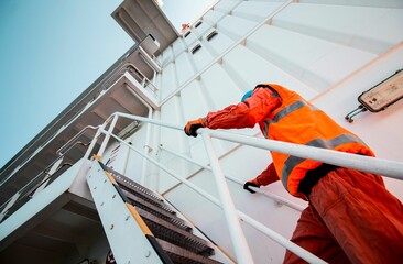 Construction worker wearing an orange vest is climbing a staircase - obrazy, fototapety, plakaty