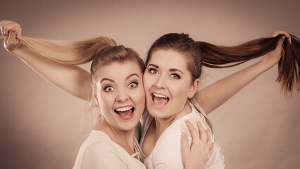 Two happy friends women hugging holding hair
