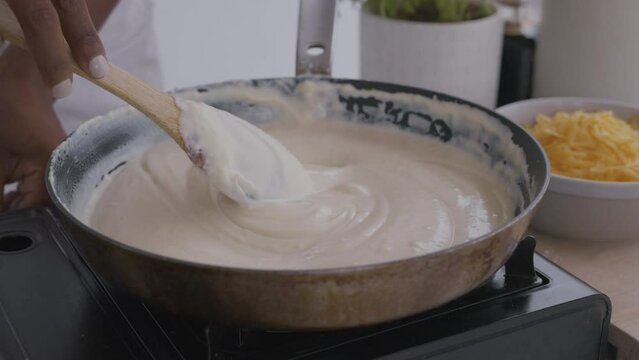 Woman making béchamel sauce. Stirring in pan with wooden spoon. Béchamel for macaroni and cheese or lasagne. Beautiful kitchen homemade food. Medium close-up shot in 4k, 50 or 25 frames per second. 