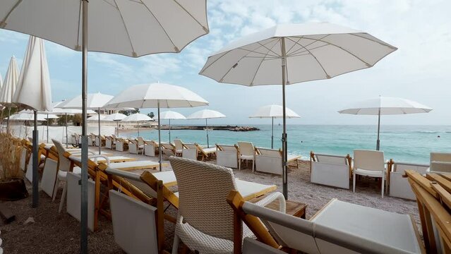 The famous beach Larvotto of principality of Monaco in sunny day, sun umbrellas, palm trees, azure water