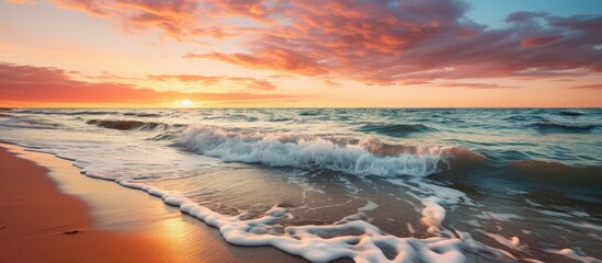 At sunset the sandy beach along the Baltic Sea is being inundated by gentle waves - obrazy, fototapety, plakaty
