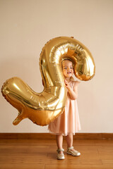 Little girl stands in a room with an inflatable number two in her hands