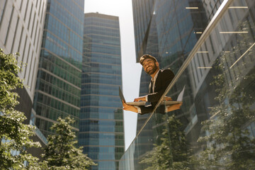 Stylish male manager working on laptop standig on office terrace and looks away. High quality photo