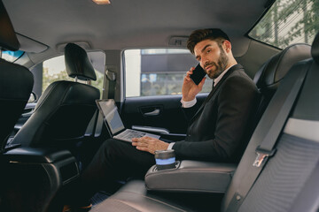 Busy entrepreneur working on laptop and talking on phone while going to airport by car