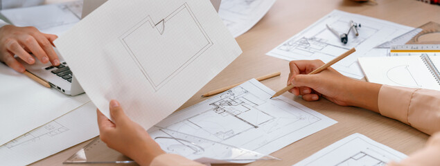 Skilled architect drafts blueprint on paper while male engineer works on laptop in architectural...