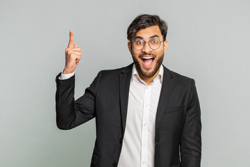 Eureka. Inspired Indian businessman pointing finger up with open mouth, having good idea, plan, startup, showing inspiration motivation gesture, problem solution. Arabian man on gray background