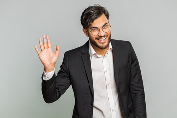Indian businessman smiling friendly at camera, waving hands gesturing hello greeting or goodbye welcoming with invitation hospitable expression. Arabian Hindu man isolated on gray studio background