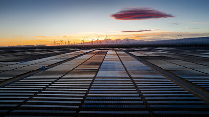 Sunset over a solar farm, wind farm in the background.