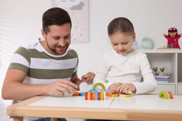 Motor skills development. Father helping his daughter to play with colorful wooden arcs at white...