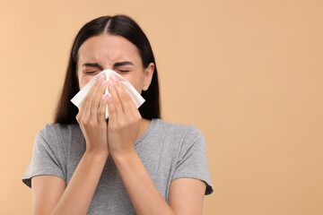 Suffering from allergy. Young woman blowing her nose in tissue on beige background. Space for text - Powered by Adobe