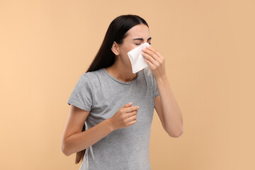 Suffering from allergy. Young woman blowing her nose in tissue on beige background