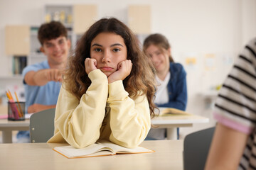 Teen problems. Lonely girl sitting separately from other students in classroom