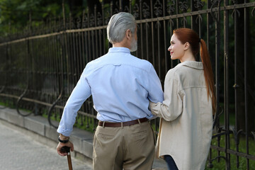 Senior man with walking cane and young woman outdoors, back view