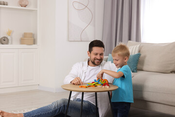 Motor skills development. Happy father helping his son to play with colorful wooden arcs at coffee table in room. Space for text