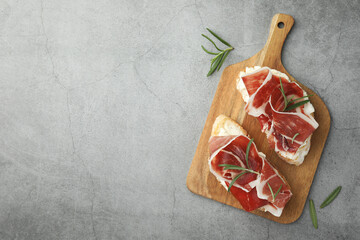 Tasty sandwiches with cured ham and rosemary on grey table, flat lay. Space for text