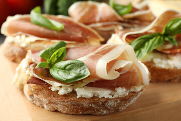 Tasty sandwiches with cured ham and basil on wooden board, closeup