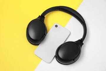 Modern wireless headphones and smartphone on color background, above view