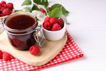 Jar of delicious raspberry jam, fresh berries and green leaves on white wooden table. Space for text