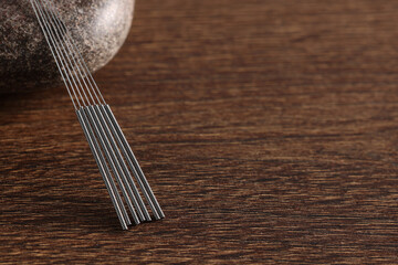Acupuncture needles and spa stone on wooden table, closeup. Space for text