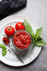 Jar of tasty tomato paste and ingredients on gray table, top view