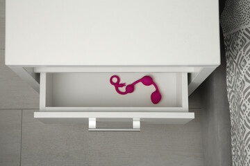 Pink anal balls in open drawer of bedside table indoors, above view. Sex toy