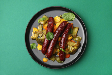 Delicious smoked sausage and baked vegetables on green background, top view
